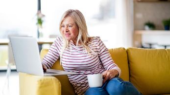 Ältere Frau sitzt mit Kaffeetasse vor Laptop ©  Unsplash+ 