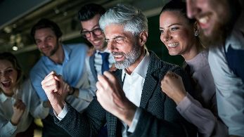 Gruppe von Personen jubelt vor einem Laptop ©  Unsplash+ 