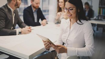 Frau lächelnd in Konferenzraum mit Tablet in den Händen ©  Unsplash+ 