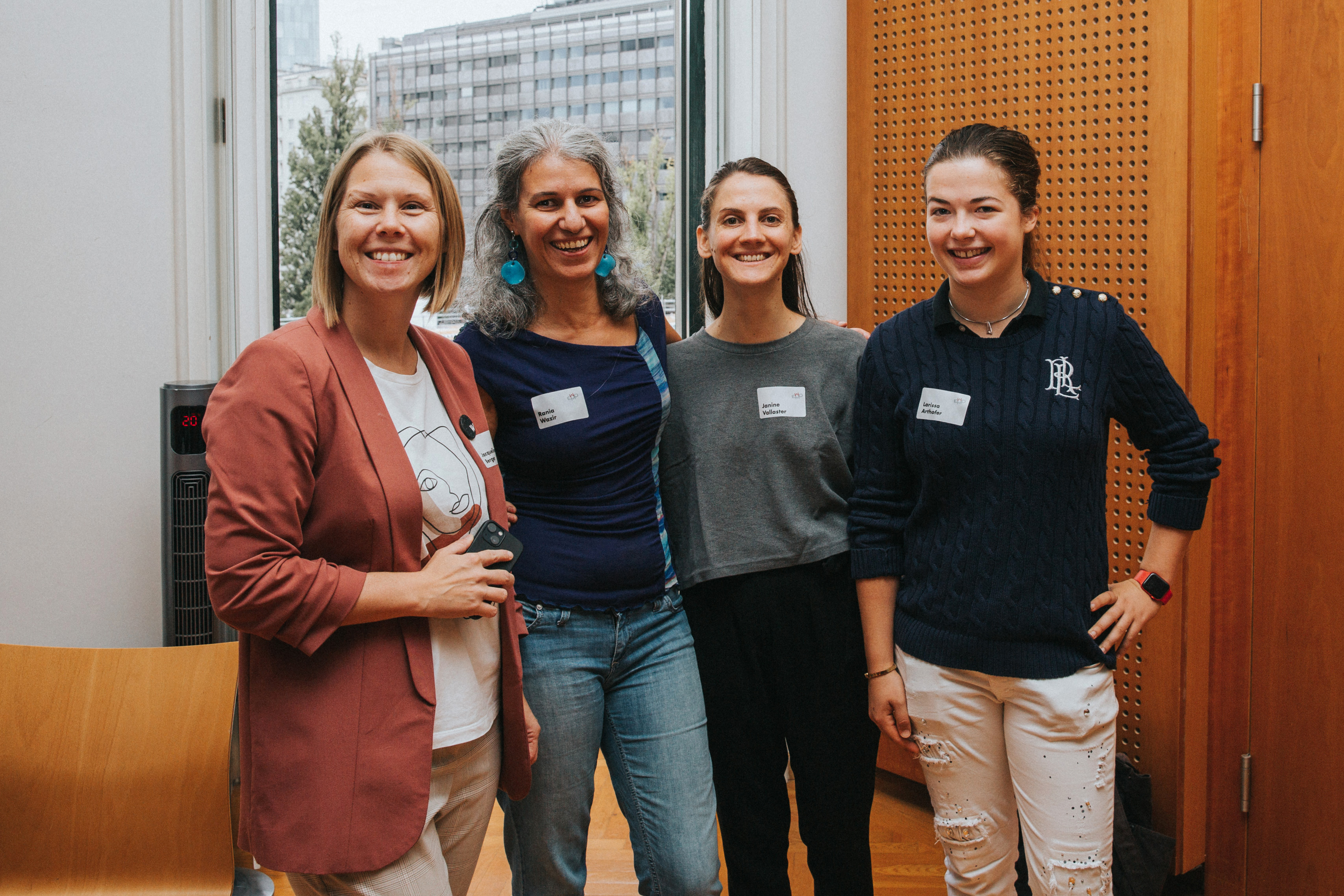 Zu sehen sind vier Frauen, die gemeinsam in die Kamera lächeln. Im Hintergrund ist ein großes Fenster zu sehen und auf der rechten Seite große Holz-Paneele. © Kathrin Hanga 