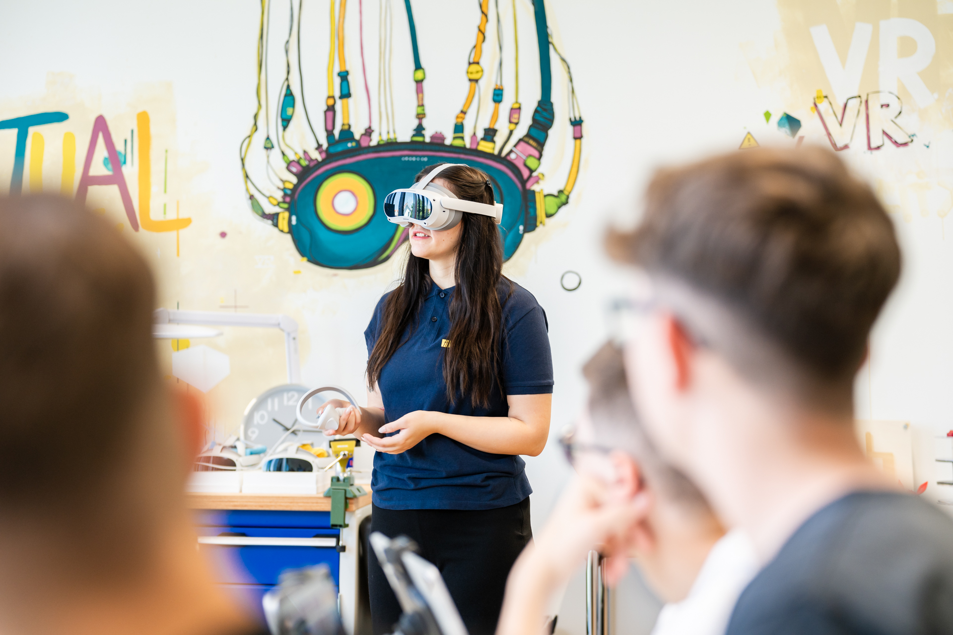 Eine junge Frau trägt eine Virtual Reality-Brille und einen Controller in der Hand. Einige andere Zuschauerinnen und Zuschauer sehen ihr dabei zu. © Klaus Ranger 