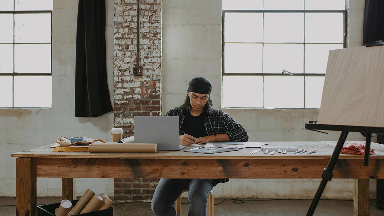 Mann sitzt auf einem Tisch mit Laptop und künstlerischem Werkzeug ©  Surface  - Unsplash 