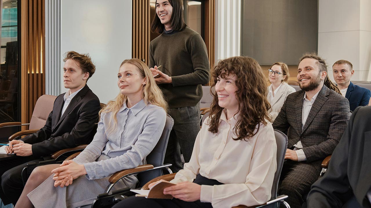 Personengruppe auf Konferenz sitzt lächelnd auf Stühlen ©  Unsplash+ 