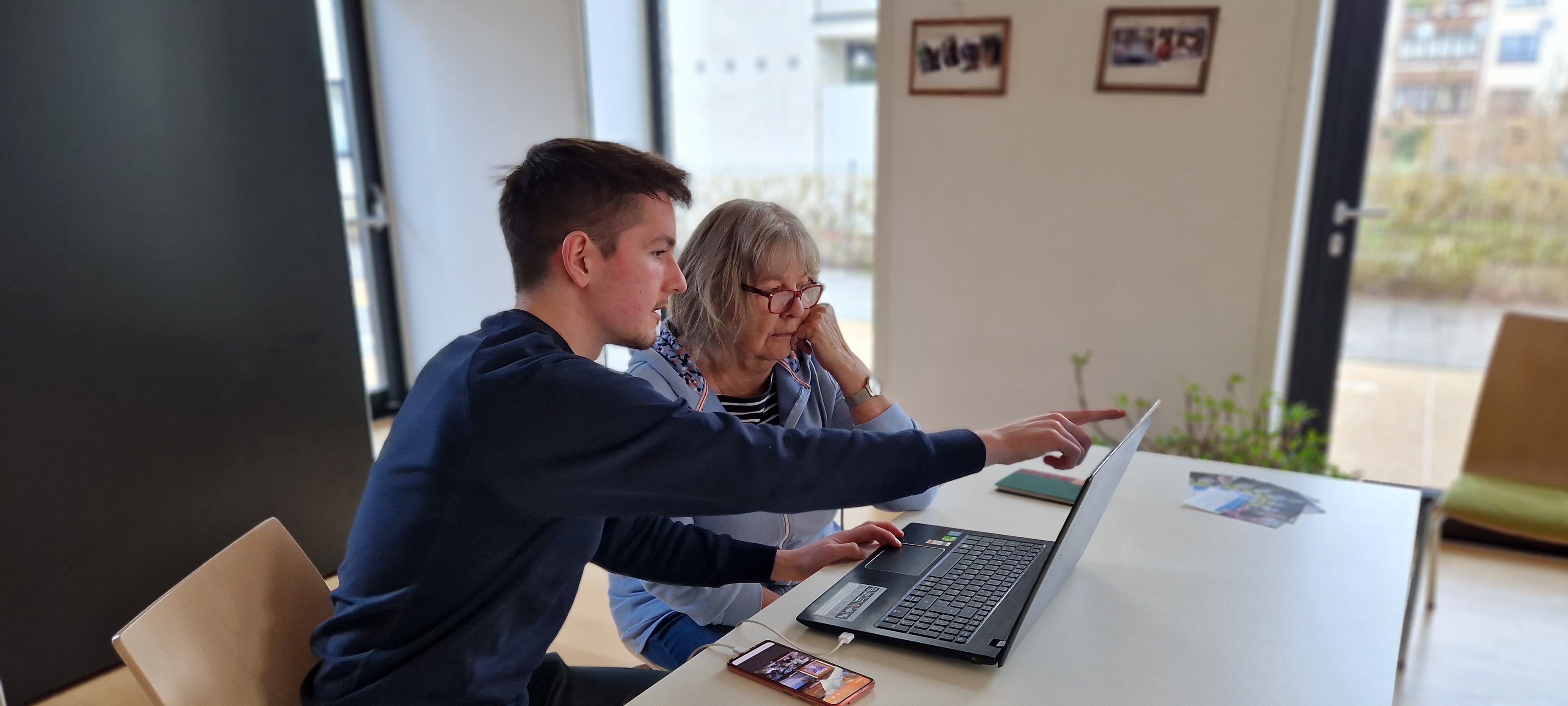 Ein junger Mann und eine ältere Frau sitzen in einem Büro vor einem Laptop, er erklärt ihr etwas.  © Diakoniewerk  - Diakoniewerk 