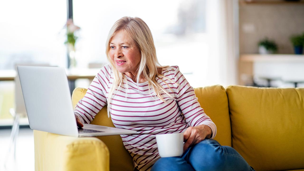 Ältere Frau sitzt mit Kaffeetasse vor Laptop © Unsplash+