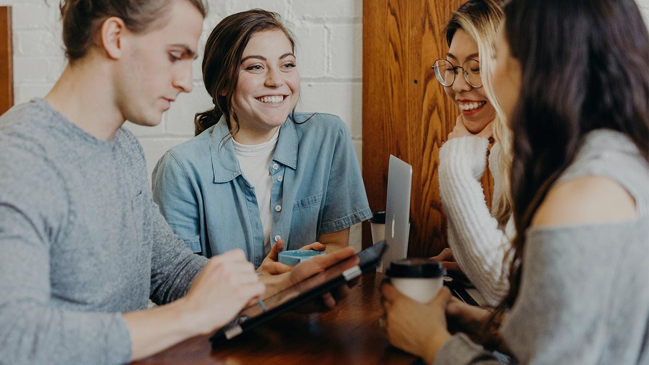 Gruppe von Personen steht an einem Tisch und unterhält sich, während eine Person ein Tablet in der Hand hält ©  Brooke Cagle  - Unsplash 