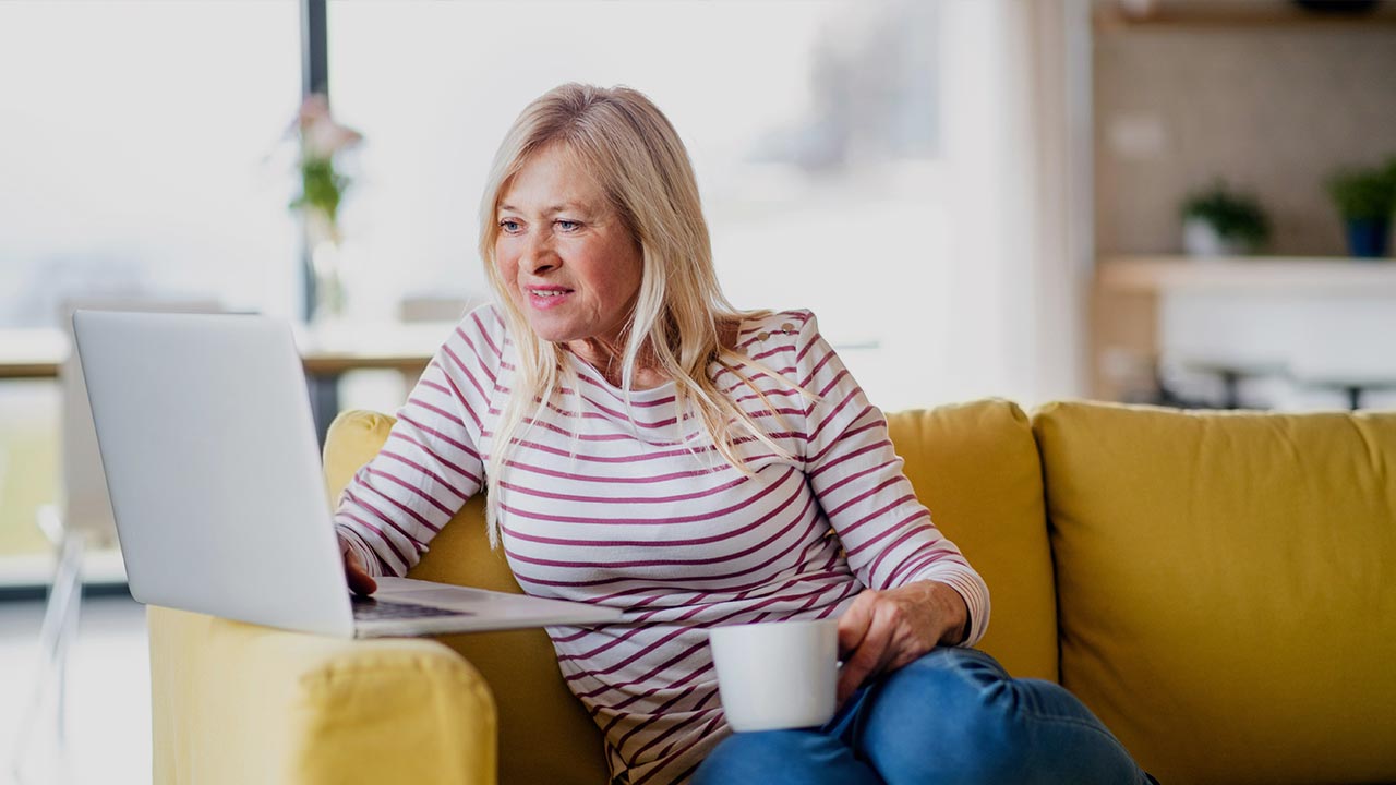 Seniorin sitzt lächelnd vor Laptop ©  Unsplash+ 