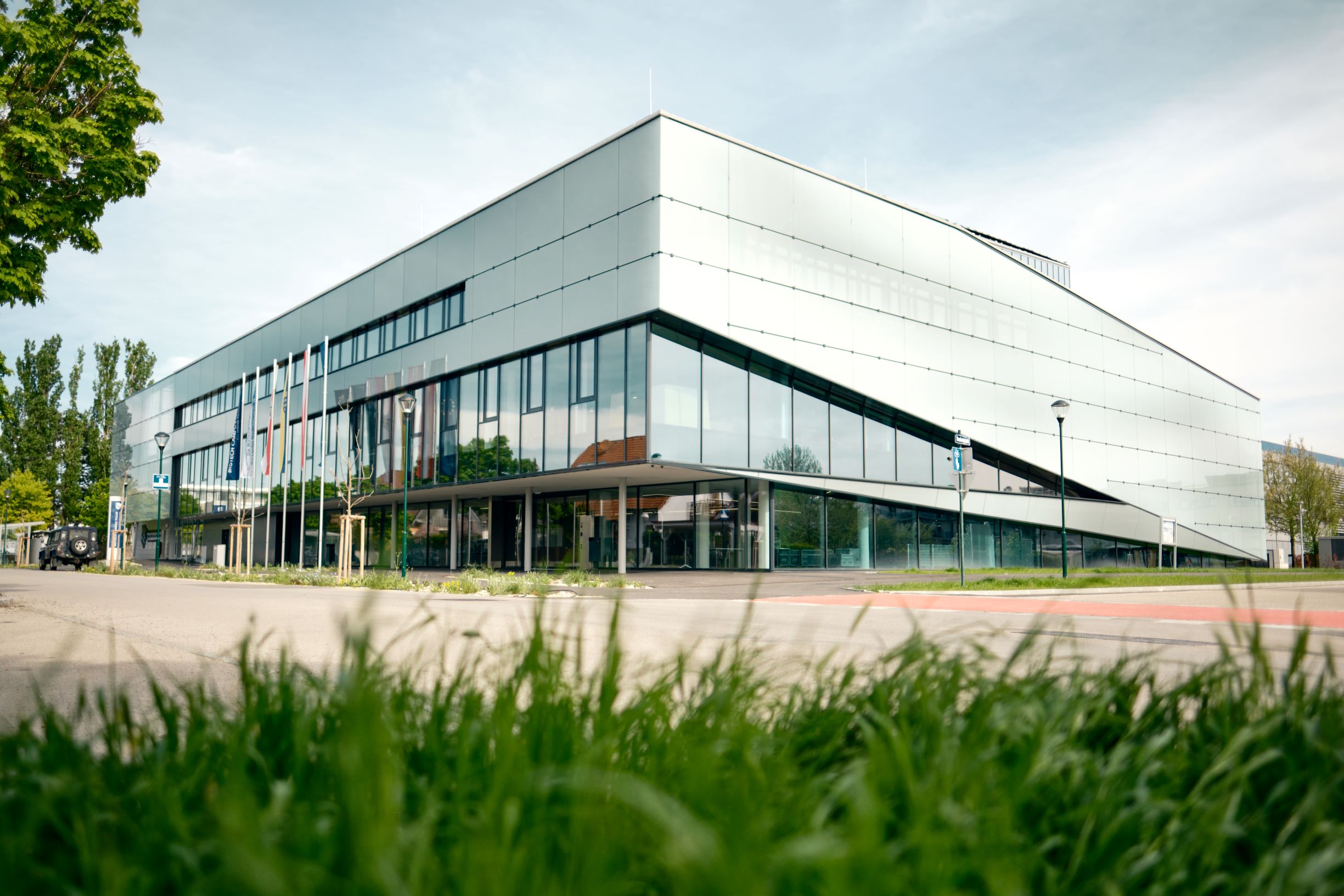 Das Bild zeigt das Haus der Digitalisierung von außen, ein modernes Gebäude aus Glas, davor sieht man eine Parkplatz und Wiese