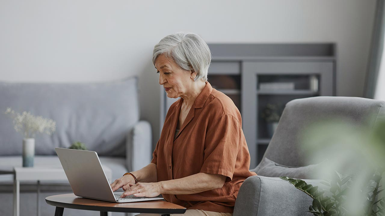 Seniorin sitzt lächelnd vor einem Laptop © Unsplash+