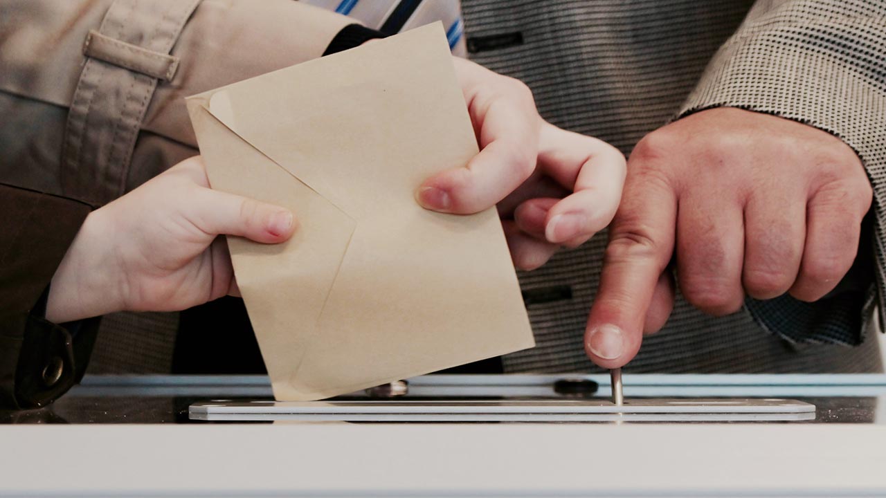 Drei Hände, die einen Stimmzettel in eine Box werfen ©  Arnaud Jaegers  - Unsplash 
