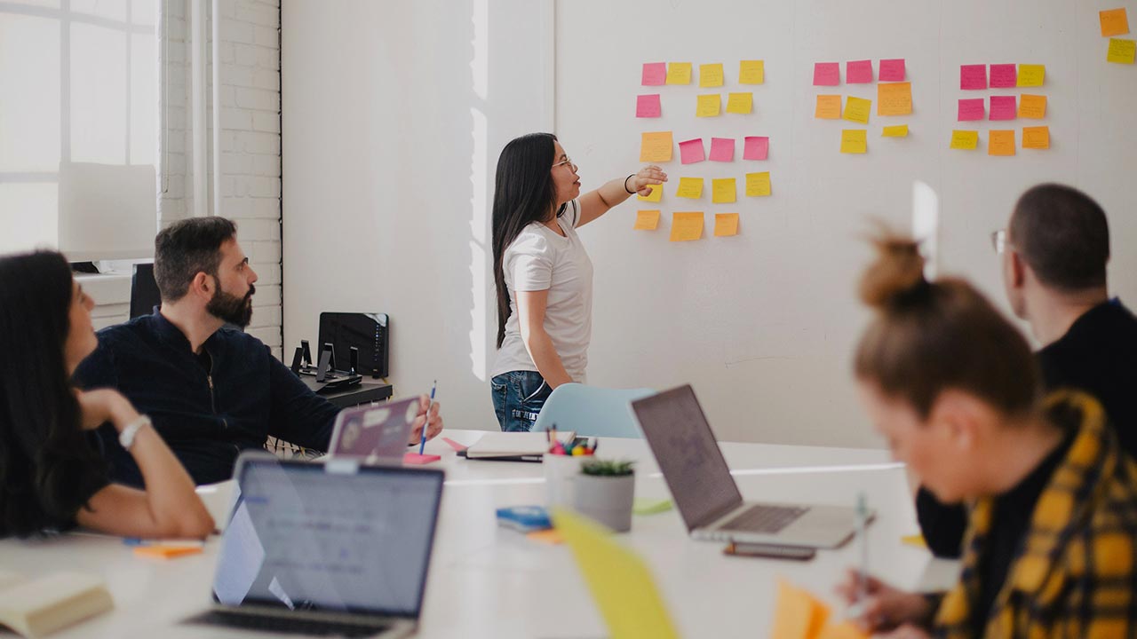 Frau steht vor einem Whiteboard und unterrichtet eine Gruppe von Personen © Jason Goodman - Unsplash