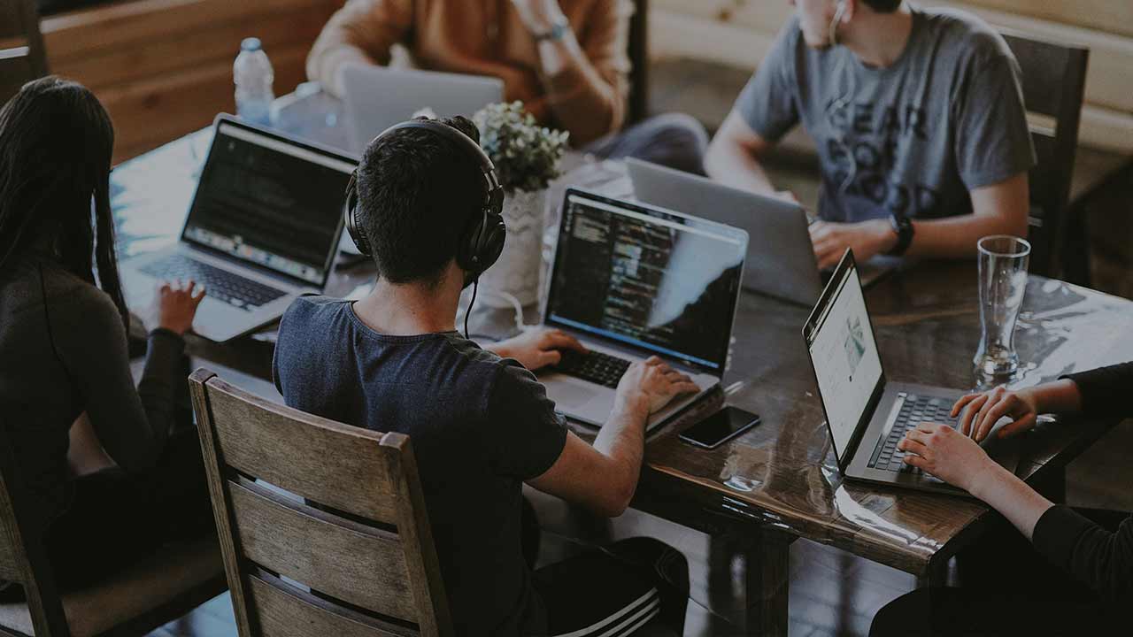 Mehrere Personen sitzen an einem Tisch und arbeiten am Laptop ©  Unsplash+ 