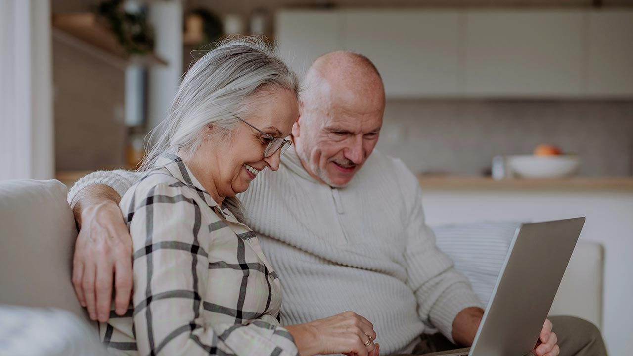 Ein Mann und eine Frau sitzen lachend vor einem Laptop © Unsplash+